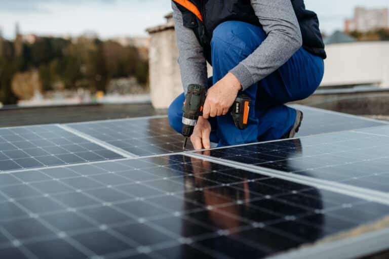 Solar panel technician with drill installing DIY solar panels on roof on family house a sunny day High quality photo